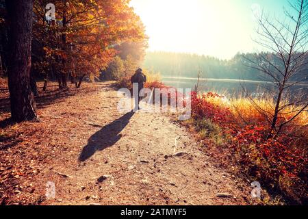 Uomo turistico sorge su una pittoresca riva del lago nella mattina d'autunno e guardando l'alba Foto Stock