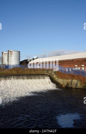 Weir sul fiume irwell con edifici industriali e silos in background a radcliffe, Bury lancashire uk Foto Stock