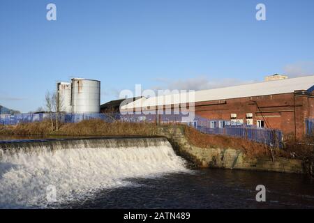 Weir sul fiume irwell con edifici industriali e silos in background a radcliffe, Bury lancashire uk Foto Stock