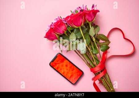 Bouquet di rose rosa con arco a forma di hart e telefono cellulare con schermo di copia Foto Stock