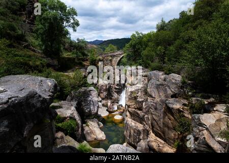 Vista sull'antico Ponte Mizarela (o Ponte del Diavolo) con cascata, presso il Parco Nazionale di Peneda Geres, in Portogallo, in Europa Foto Stock