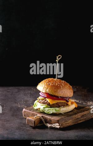 Hamburger fresco fatto in casa su tagliere di legno su sfondo scuro Foto Stock