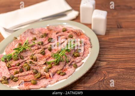 Manzo cotto in suvid. E' tagliato a fette sottili e decorato con capperi e microgreen. Su sfondo di legno in un piatto ovale. Spazio di copia Foto Stock