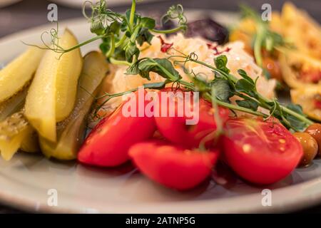 Verdure fermentate, salate ed erbe. Ingredienti per l'insalata. Cetrioli, pomodori, olive, crauti, prugne. A fette, decorato microgreen. Su un Foto Stock