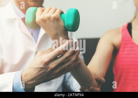 fisioterapia - fisioterapista aiutare la paziente della donna a recuperare dalla ferita della mano a casa. esercizi dumbbell Foto Stock