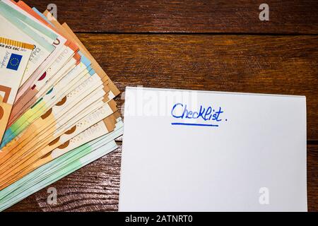 Lista di controllo di testo su carta e euro soldi sul tavolo. Pianificazione del risparmio o del concetto di business. Foto Stock