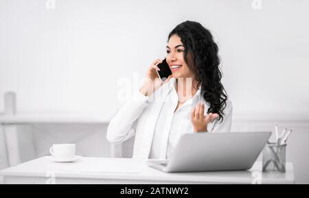 Sorridente ragazza ispanica che parla al telefono in ufficio Foto Stock