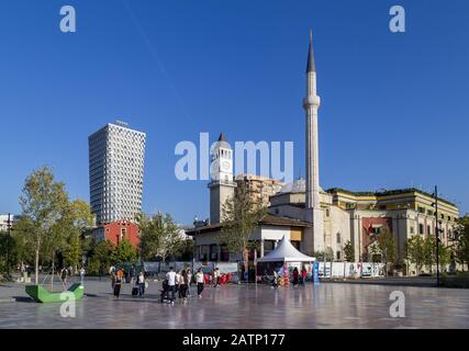 La piazza principale di Tirana con la Moschea di He Et'Hem Bey, la torre dell'orologio ottomano, il moderno edificio alberghiero e la bandiera nazionale, Foto Stock