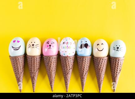 Fila di uova di Pasqua dipinte a mano in coni di waffle su uno sfondo giallo. Concetto di uovo di Pasqua. Foto Stock