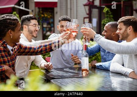 Un gruppo di amici maschi che hanno un brindisi celebrativo insieme all'aperto in una birreria all'aperto della città. Foto Stock