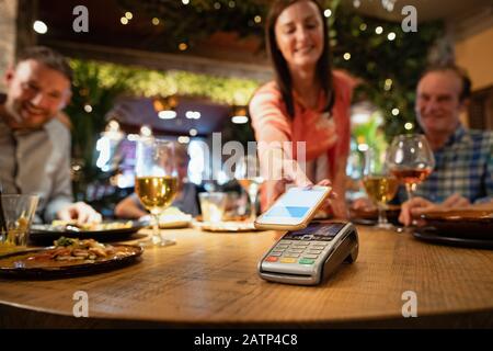 Una donna che paga per un pasto utilizzando il pagamento senza contatto attraverso il suo telefono. Foto Stock