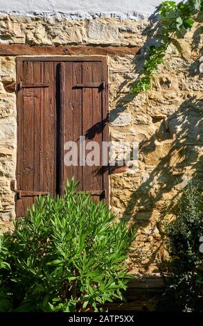 La vista della vecchia finestra con persiane in legno chiuso nel muro della casa in pietra nel villaggio di Lania. Limassol. Foto Stock