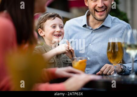 Una famiglia multi-generazione che beve insieme all'aperto in un bar, il punto principale è il ragazzo giovane ridere. Foto Stock