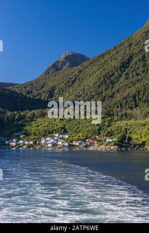 Scia del traghetto Quelat che lascia il villaggio di Puerto Gaviota a Isla Magdalena, montagne coperte di foresta pluviale temperata, regione di Aysen, Patagonia, Cile Foto Stock