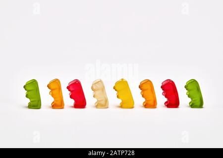 Gli orsi gommosi colorati camminano in linea o aspettano in coda su sfondo bianco con spazio di copia Foto Stock