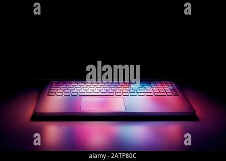 Schermo del computer portatile a mezza apertura che riflette le luci colorate sulla tastiera su sfondo nero. Foto Stock