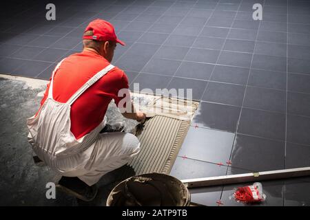 Un lavoratore edile mettendo sul nuovo pavimento di piastrelle. Foto Stock