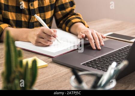 lo studio è il potere. mani da vicino di una donna d'affari, studente o freelancer in camicia gialla prendere appunti nel suo notebook durante la navigazione in internet Foto Stock