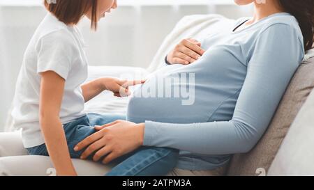 Piccola ragazza curiosa che la tocca aspettandosi la pancia grande della madre Foto Stock