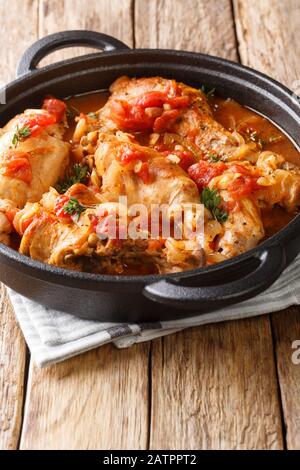 Coniglio brasato in salsa di pomodoro con vino bianco ed erbe primo piano in una padella sul tavolo. Verticale Foto Stock