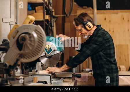 Vista laterale dell'artigiano con sega circolare su tavola di legno in officina Foto Stock