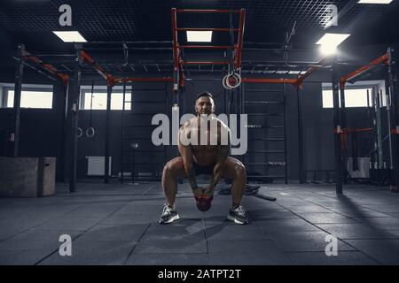 Inarrestabile. Giovane atleta caucasico muscolare praticando squat in palestra con il peso. Modello maschile fare esercizi di forza, formazione corpo inferiore. Benessere, stile di vita sano, concetto di bodybuilding. Foto Stock