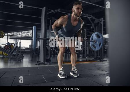 Potente. Giovane atleta caucasico muscolare che pratica pull-up in palestra con barbell. Modello maschile fare esercizi di forza, formazione del corpo superiore. Benessere, stile di vita sano, concetto di bodybuilding. Foto Stock