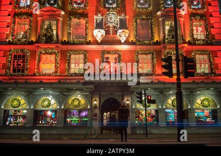 Fortnum e Mason fanno acquisti su Piccadilly con il suo display Christmas Light con i fari a lunga esposizione che passano in primo piano. Londra Foto Stock