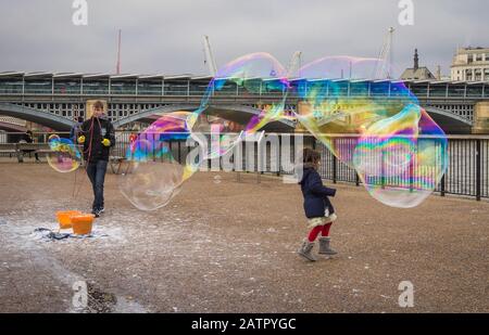 Artista di strada sulla riva sud del Tamigi che fa grandi bolle con un bambino che gioca sotto. Londra Foto Stock