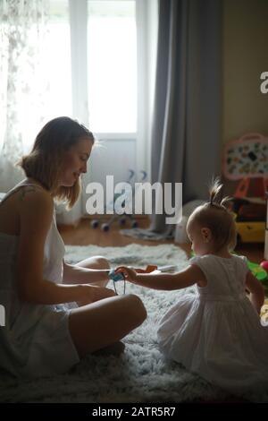 La madre gioca con la figlia piccola nella stanza sul tappeto. Foto Stock
