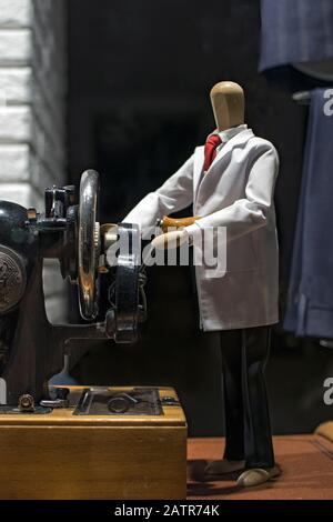 Una figurina di un uomo di legno, in un mantello bianco che si stringe alla ruota di una macchina da cucire. Il concetto di vendita, design, abbigliamento stilista, sartori Foto Stock