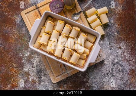 Pasta cruda farcita con carne macinata in una pentola di ceramica su un tagliere di legno. Cannelloni italiani. Cucina Mediterranea Tradizionale. Vista dall'alto Foto Stock