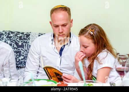 Famiglia intorno al tavolo per la tradizionale cena di Pasqua leggendo l'Haggadah. Famiglia ebraica alla festa di Pasqua. Attenzione selettiva all'uomo. Foto Stock