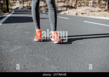 Donna sportiva in scarpe da running in piedi sulla strada di montagna asfaltata, da vicino sulle sneakers Foto Stock