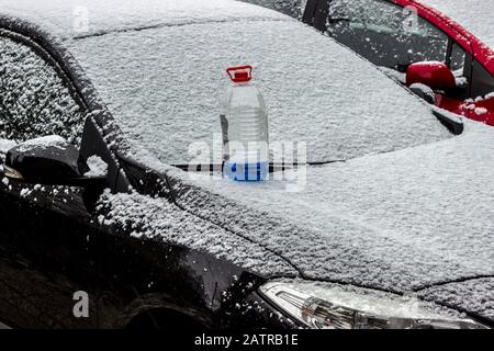 L'antigelo lavaparabrezza si trova sul cofano anteriore della vettura nera nella neve in inverno. Foto Stock