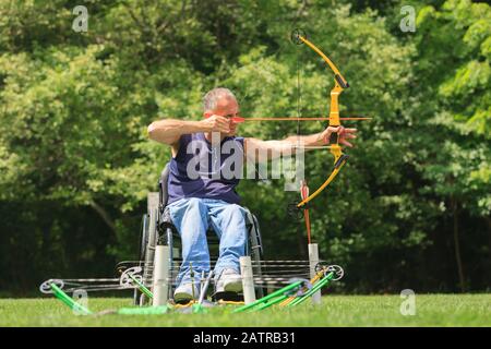 Uomo in sedia a rotelle con arco e freccia Foto Stock