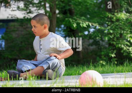 Ragazzo pre-teenager fuori seduto a terra con gli alberi dentro lo sfondo Foto Stock