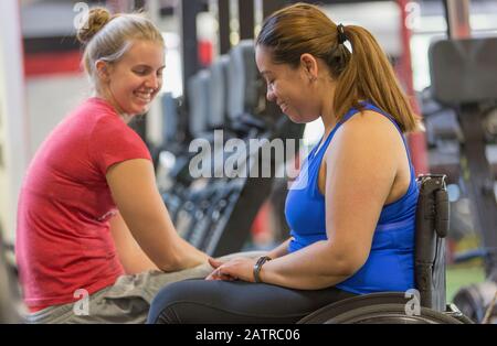 Giovane donna in sedia a rotelle che parla con un'altra giovane donna in un centro fitness Foto Stock