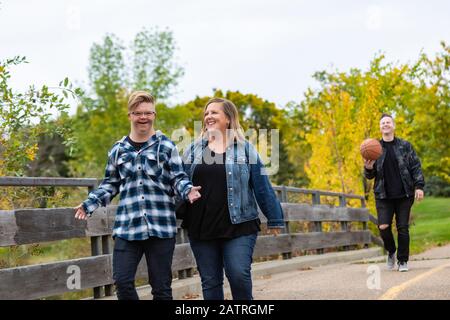 Un giovane con la sindrome di Down che cammina con suo padre e madre mentre godendo la compagnia dell'altro in una città parcheggia in una calda serata autunnale Foto Stock