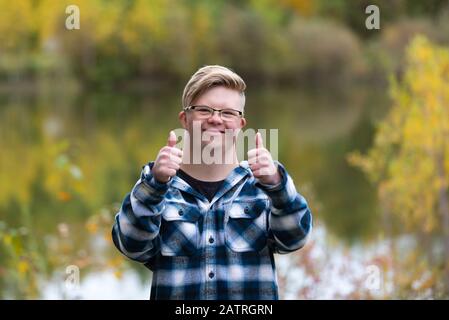 Un giovane con la sindrome di Down che dà un pollice in su in un parco della città in una calda sera di autunno: Edmonton, Alberta, Canada Foto Stock