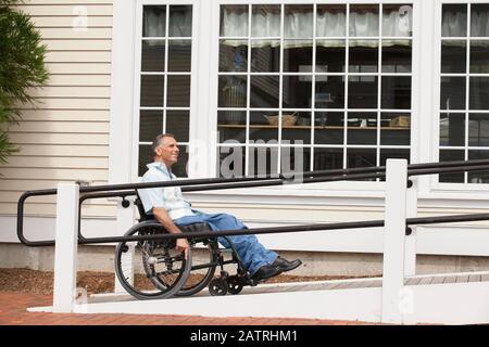 Uomo in sedia a rotelle su una rampa di accesso a un edificio Foto Stock