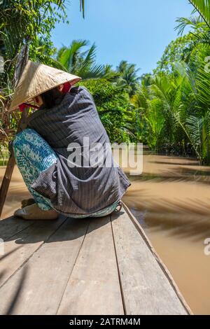 Vista posteriore di anonima donna locale che indossa tradizionale cappello a foglia pagaiando una canoa sul Delta del Mekong, Vietnam, Sud Est Asiatico Foto Stock