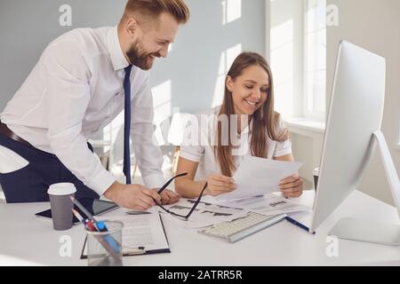 Uomo d'affari e donna d'affari positivi che lavorano sorridendo in un ufficio bianco. Foto Stock