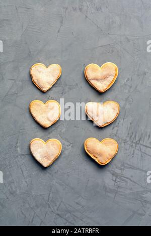 Deliziosi biscotti fatti in casa di pan di zenzero in forma di cuori disposti verticalmente in una fila su una superficie grigia in cemento, immagine con spazio di copia. Foto Stock