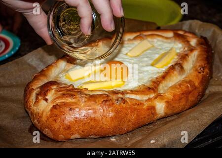 Khachapuri georgiano fresco dal forno - ciotola di pane rosolato piena di formaggio gorgogliante con burro che si fonde sulla parte superiore e un uovo crudo nel mezzo Foto Stock