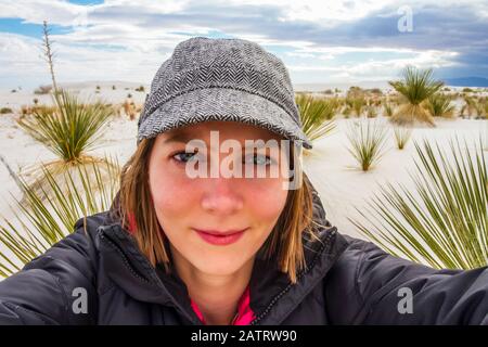 Giovane donna che prende un auto-ritratto con piante del deserto e sabbia bianca sullo sfondo, White Sands National Monument Foto Stock