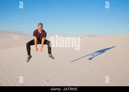 Uomo spensierato a mezz'aria sulla sabbia bianca con cielo blu, gettando un'ombra accanto a lui, White Sands National Monument Foto Stock