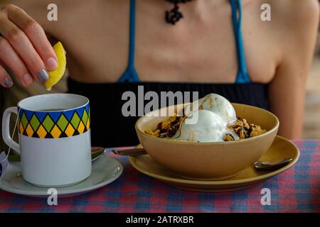 Ragazza a colazione. Una tazza di tè con gelato al limone e al cioccolato. Primo piano Foto Stock