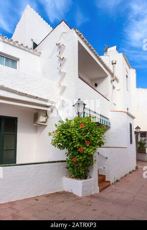 Strada con case tradizionali spagnole decorate con fiori nel villaggio di Binibeca Nou. Minorca. Spagna Foto Stock