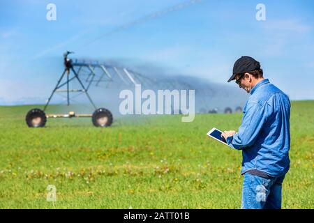 Coltivatore che usa una tavoletta su un campo di fattoria con irrigazione; Alberta, Canada Foto Stock